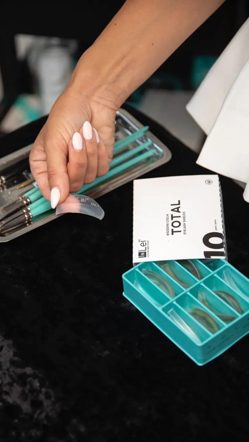 Hand mit Wimpern-Pads und Produkten während der Behandlungsvorbereitung