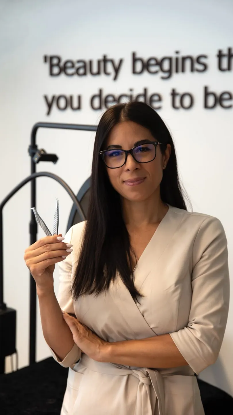 Porträt von Anita mit Wimpern-Pinzette vor der Studiowand mit Zitat